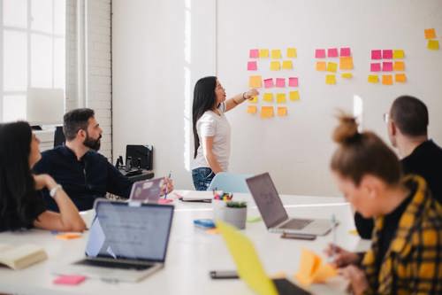 Woman explaining omnichannel marketing such as combining email and direct mail marketing on a whiteboard to a group of coworkers in a meeting